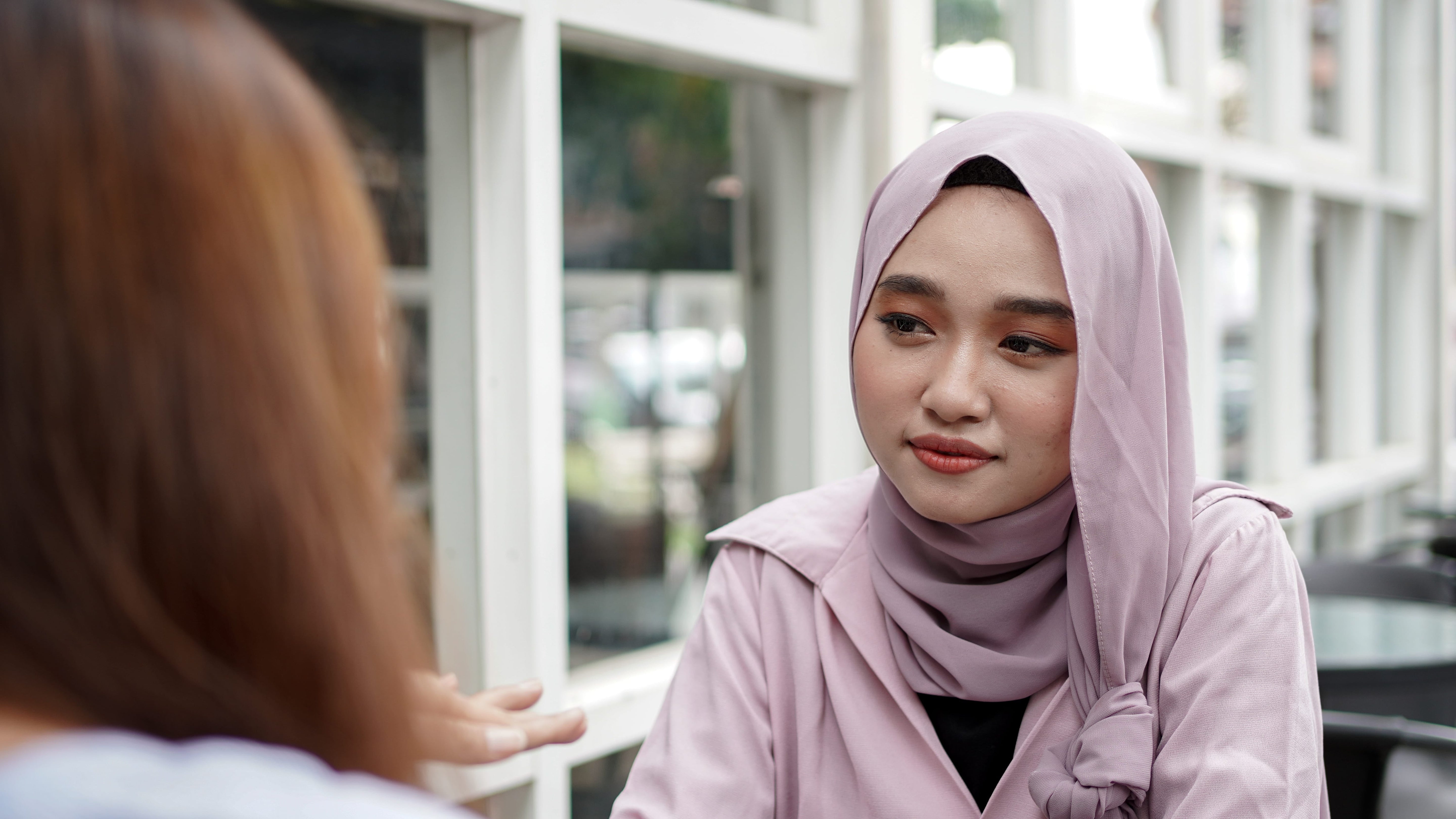 An Asian woman in a hijab talking to another woman in a café about how to maintain rebonded hair